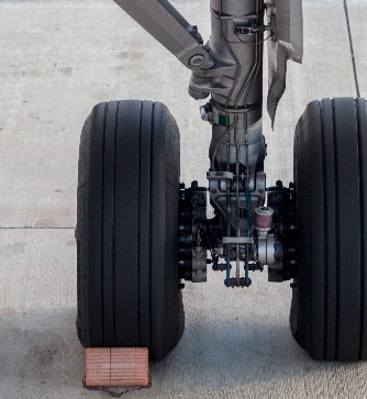 Nahaufnahme des Fahrwerks eines Flugzeugs mit zwei großen Reifen und einem Holzkeil vor einem Reifen