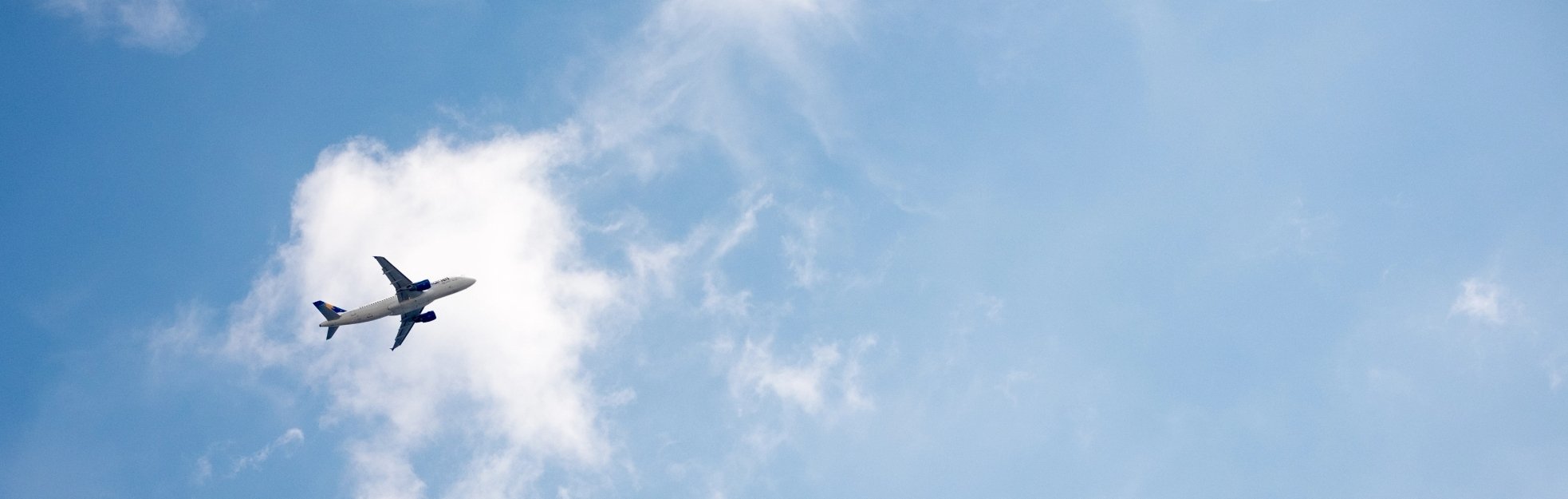 Passagierflugzeug fliegt vor blauem Himmel mit einzelnen Wolken